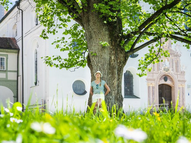 Frau lehnt entspannt am Baum vor dem Kloster Benediktbeuern